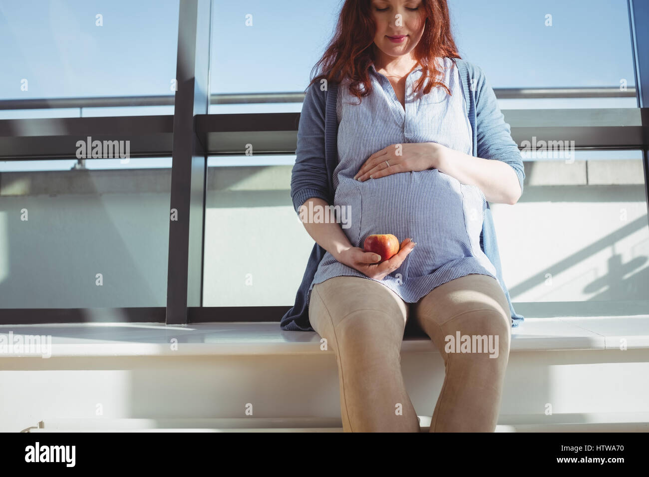 Une femme enceinte assis près de la fenêtre et holding an apple Banque D'Images