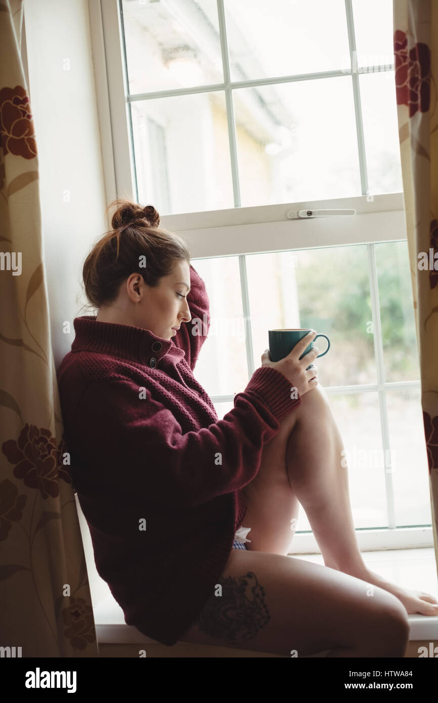 Une femme assise au rebord de fenêtre et holding Coffee cup Banque D'Images
