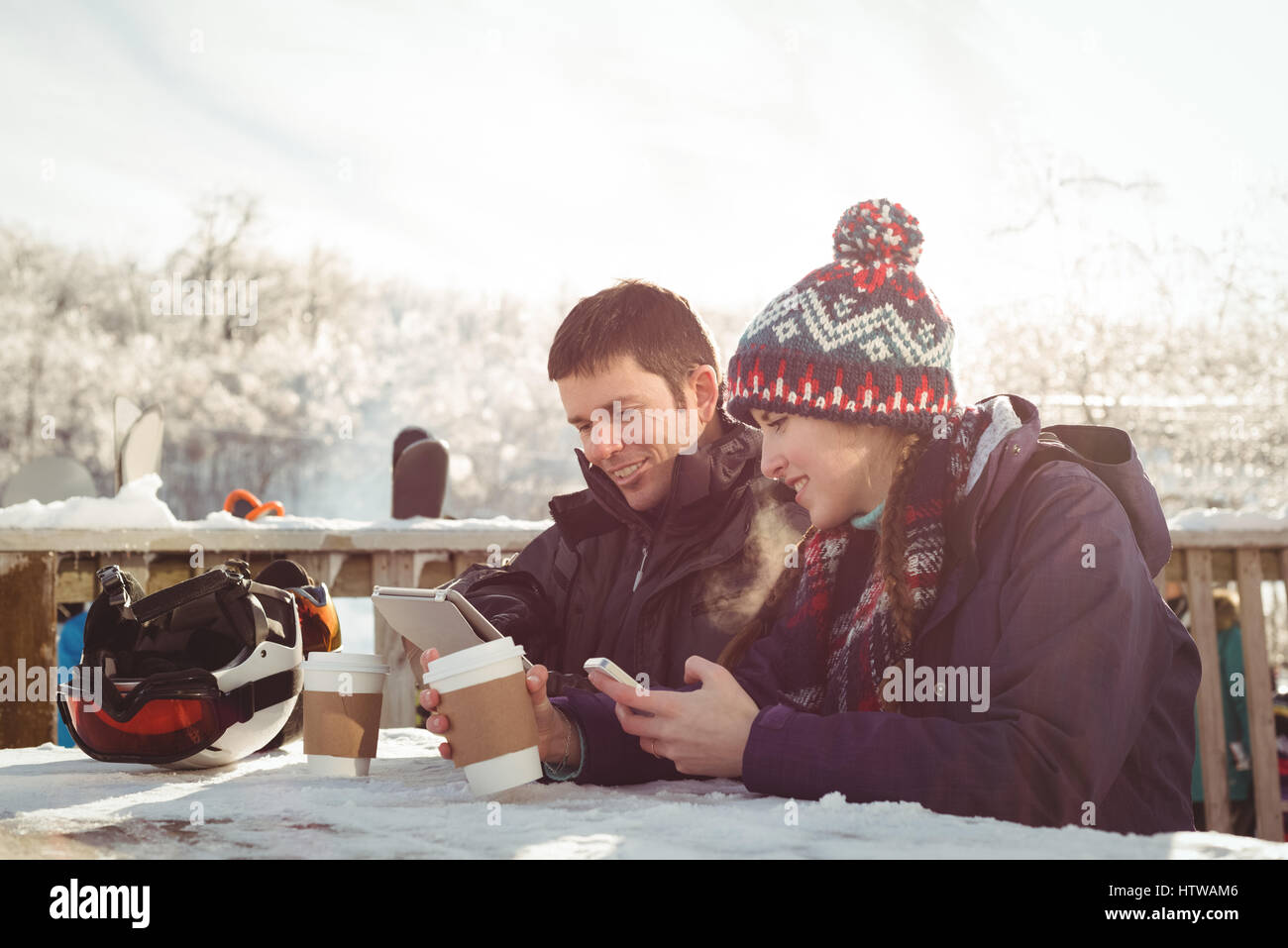 Heureux couple skieur assis à la table lors de l'utilisation de téléphone mobile et tablette numérique Banque D'Images