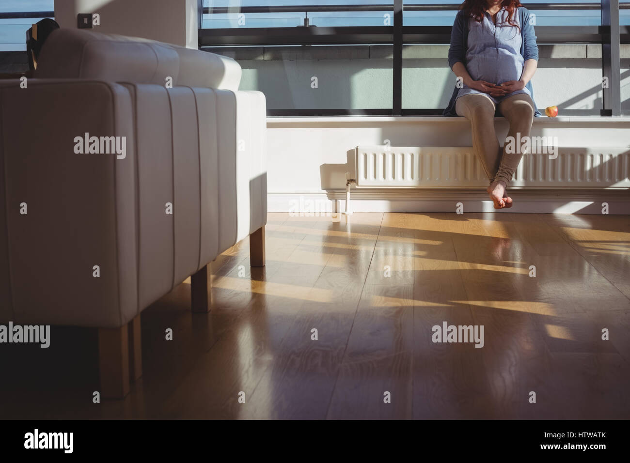 Femme enceinte assis près de fenêtre dans salle de séjour Banque D'Images