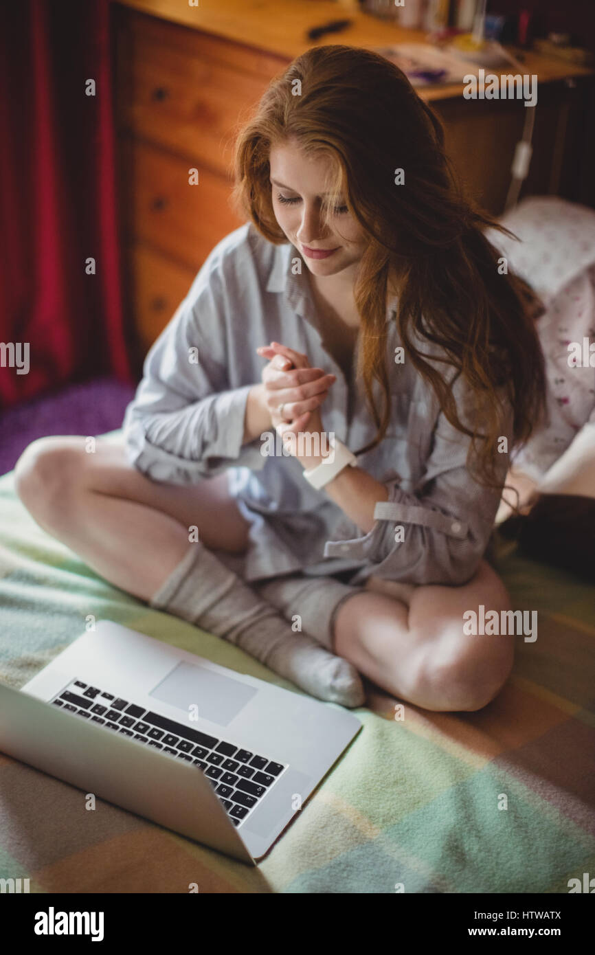 Woman with hands clasped sitting in front of laptop Banque D'Images