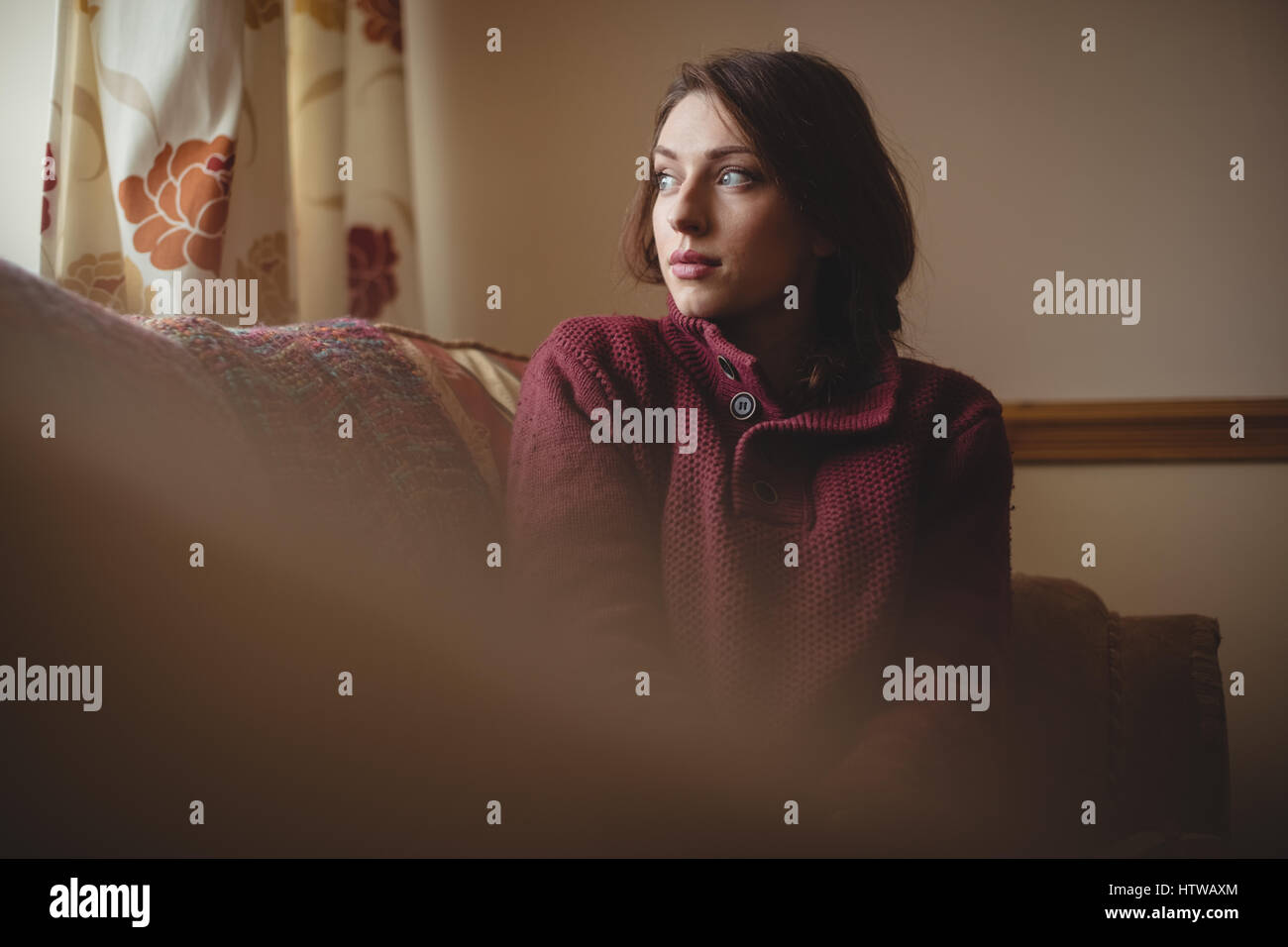 Thoughtful woman sitting on sofa in living room Banque D'Images