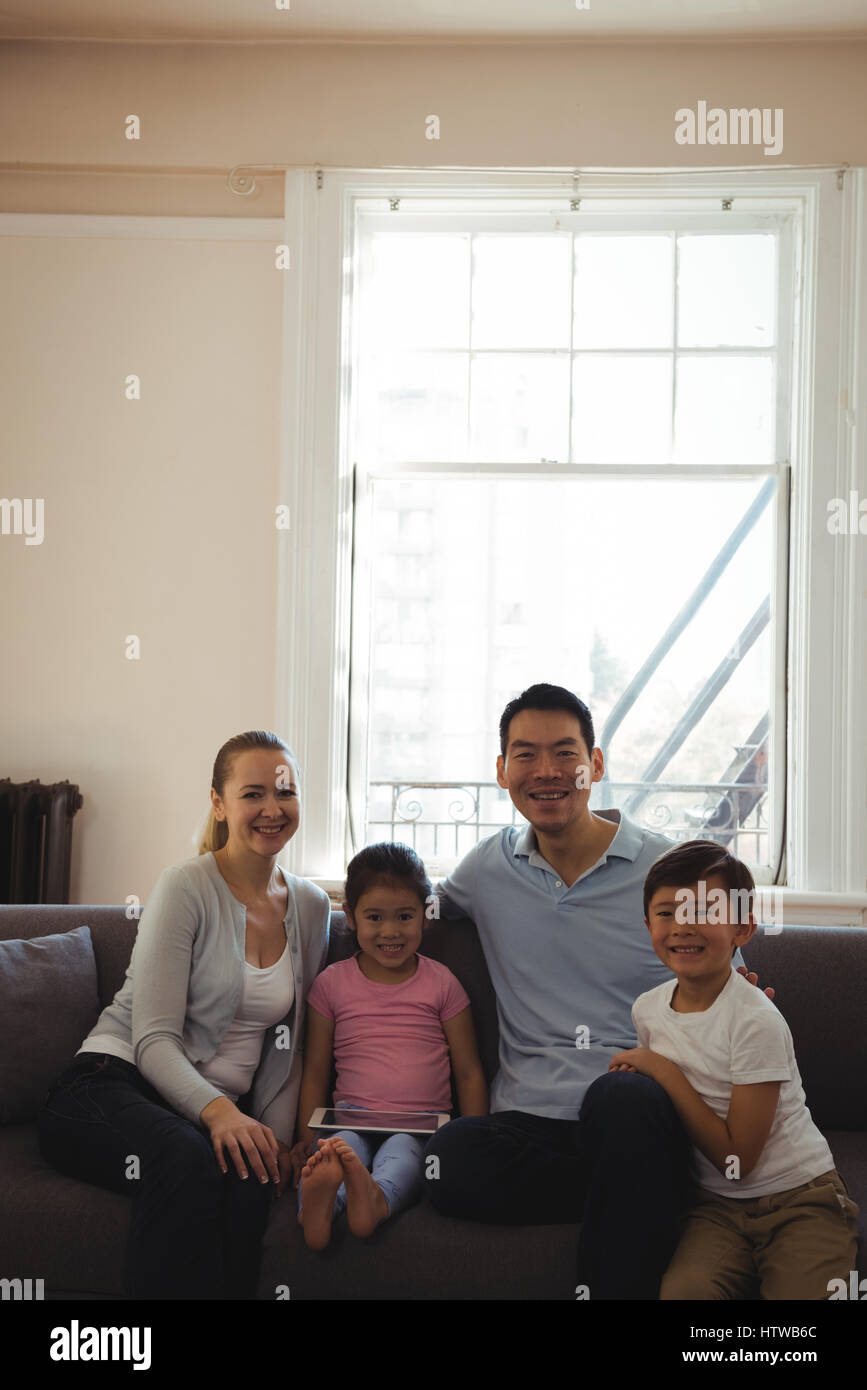 Smiling parents et enfants sitting on sofa with digital tablet in living room Banque D'Images