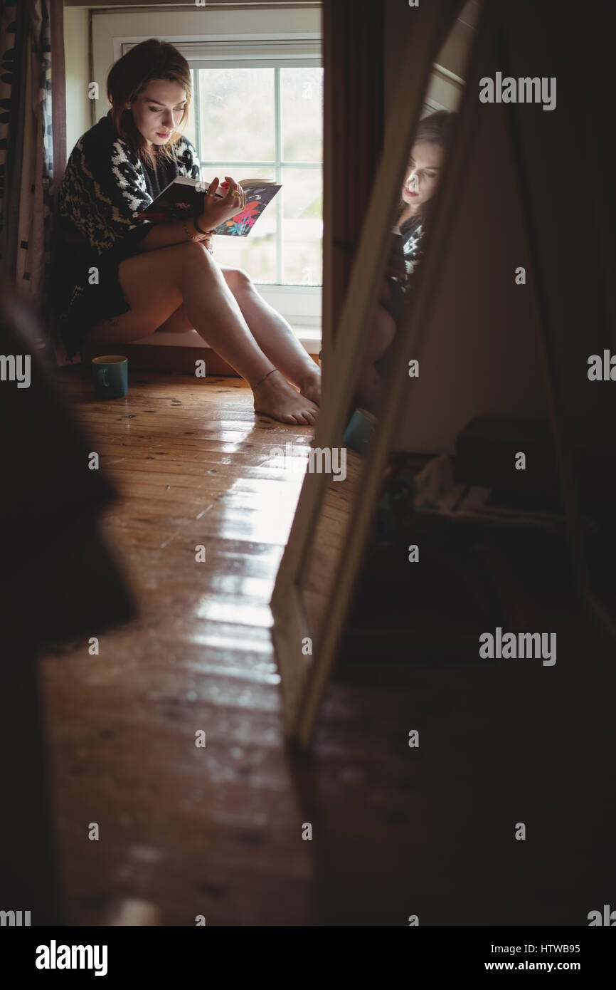 Femme assise au rebord de fenêtre et la lecture d'un livre Banque D'Images