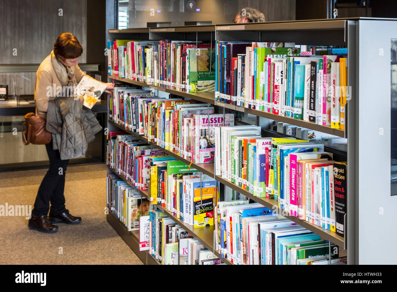 Femme choisissant livre à lire à partir de rangées de livres dans les étagères de la bibliothèque publique à Banque D'Images