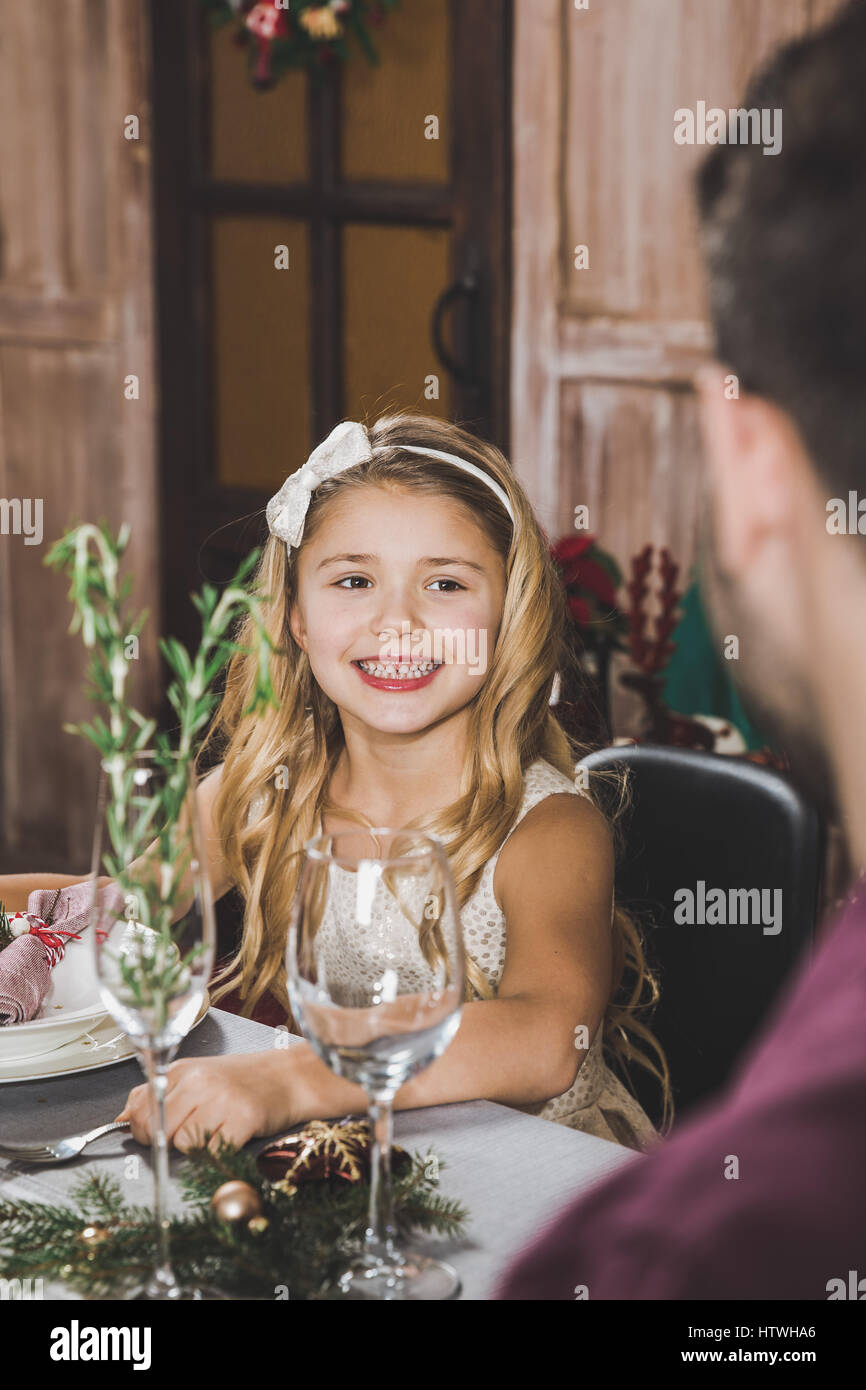 Cute smiling girl sitting at table des fêtes et à la recherche au père au moment de Noël Banque D'Images