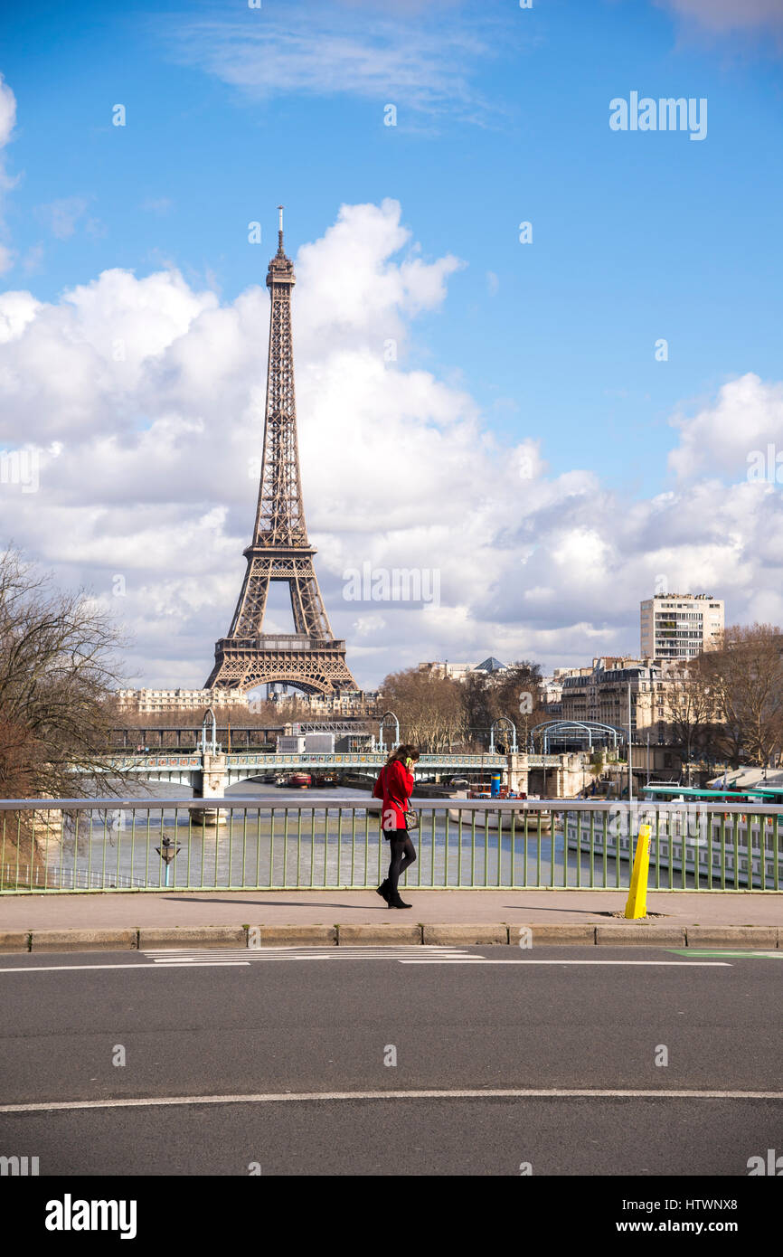 Une femme dans un manteau rouge on traverse le pont de Grenelle avec la Tour Eiffel au loin. Banque D'Images