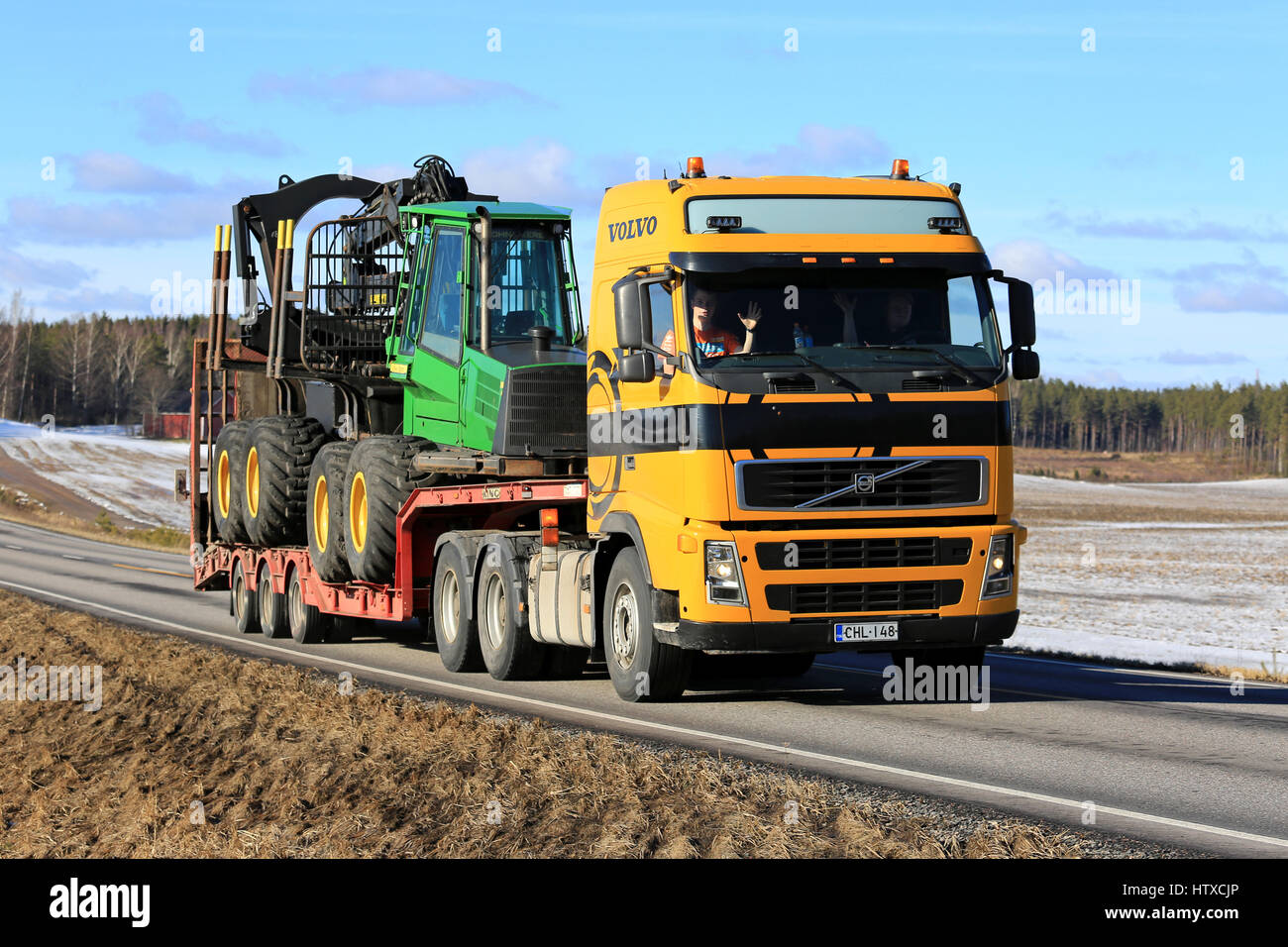 SALO, FINLANDE - le 11 mars 2017 : Volvo FH Jaune John Deere 1110 transports transitaire sur remorque forestière de cygne le long de la route sur une journée ensoleillée de sprin Banque D'Images