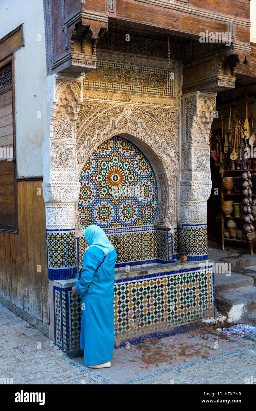 Fes, Maroc. Place Nejjarine. Femme Obtenir de l'eau à la fontaine. Banque D'Images