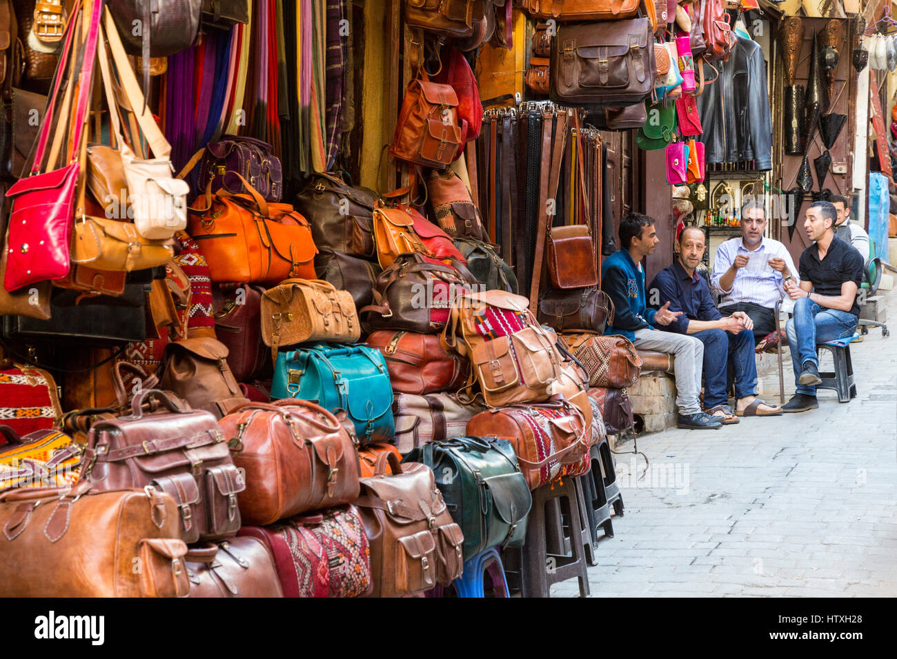 Fes, Maroc. Scène de rue à la médina. Les hommes assis à l'extérieur de magasin qui vend des articles en cuir. Banque D'Images