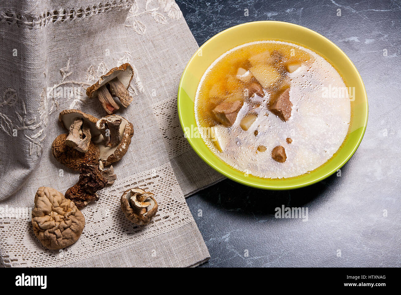 Soupe aux champignons en plaque verte sur un fond noir en noir. Cèpes séchés plusieurs champignons sauvages ou blanc sur tissu marron. Banque D'Images