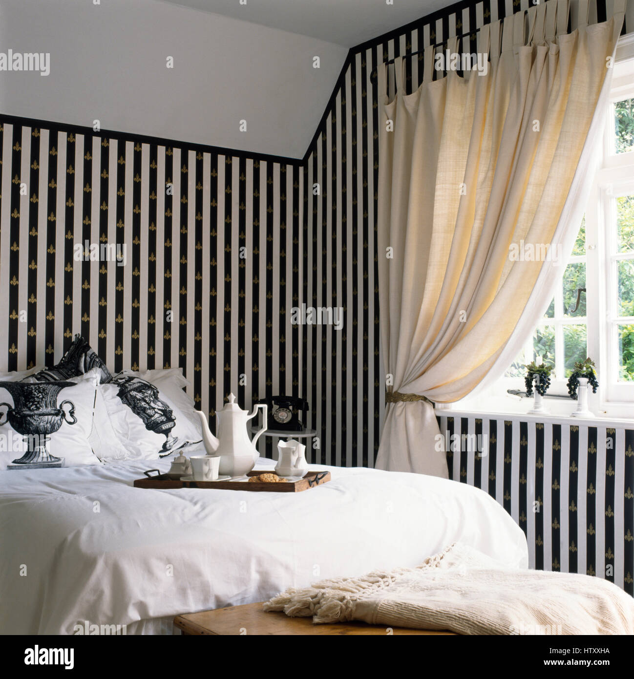 Peint en noir +bandes blanche sur mur à l'aide d'un pochoir fleur de lis d'or dans une chambre avec un plateau de petit-déjeuner et le linge blanc sur le lit Banque D'Images