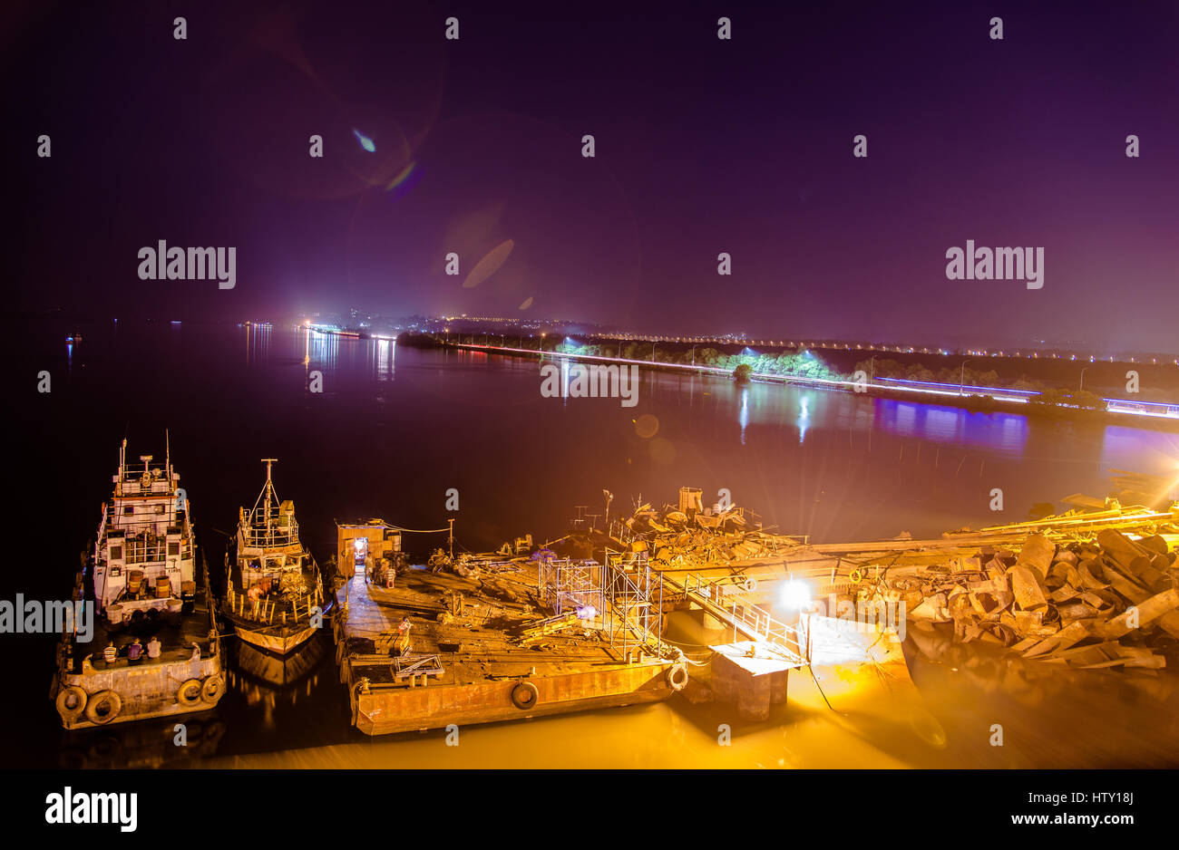 Vue de nuit sur un chantier de construction près d'une rivière et un pont sur le côté avec le trafic capturé à l'aide d'une longue exposition Banque D'Images