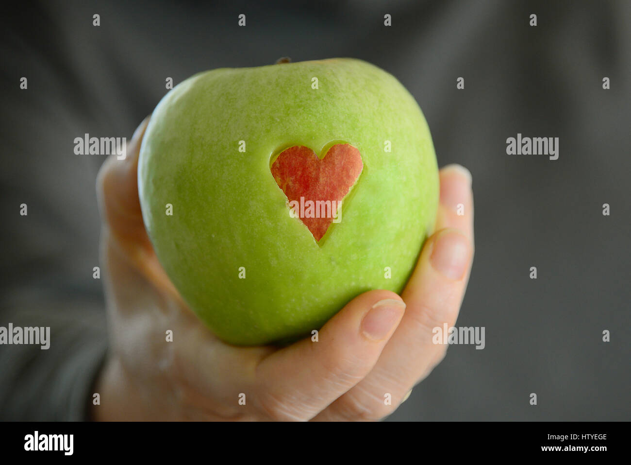 Woman's hand holding a Green Apple avec coeur rouge Banque D'Images