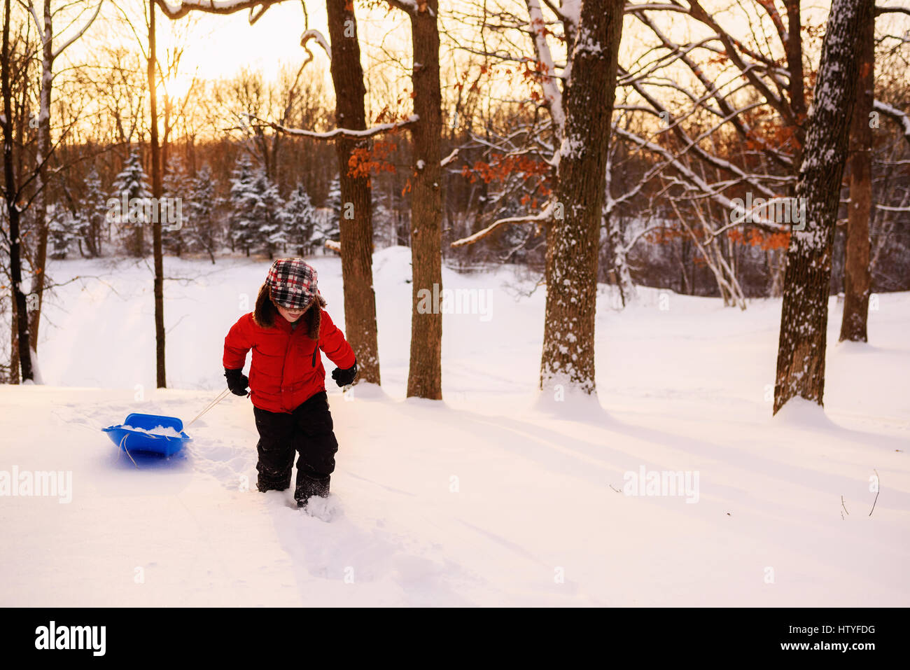 Boy pulling Sled jusqu'à une colline au coucher du soleil Banque D'Images
