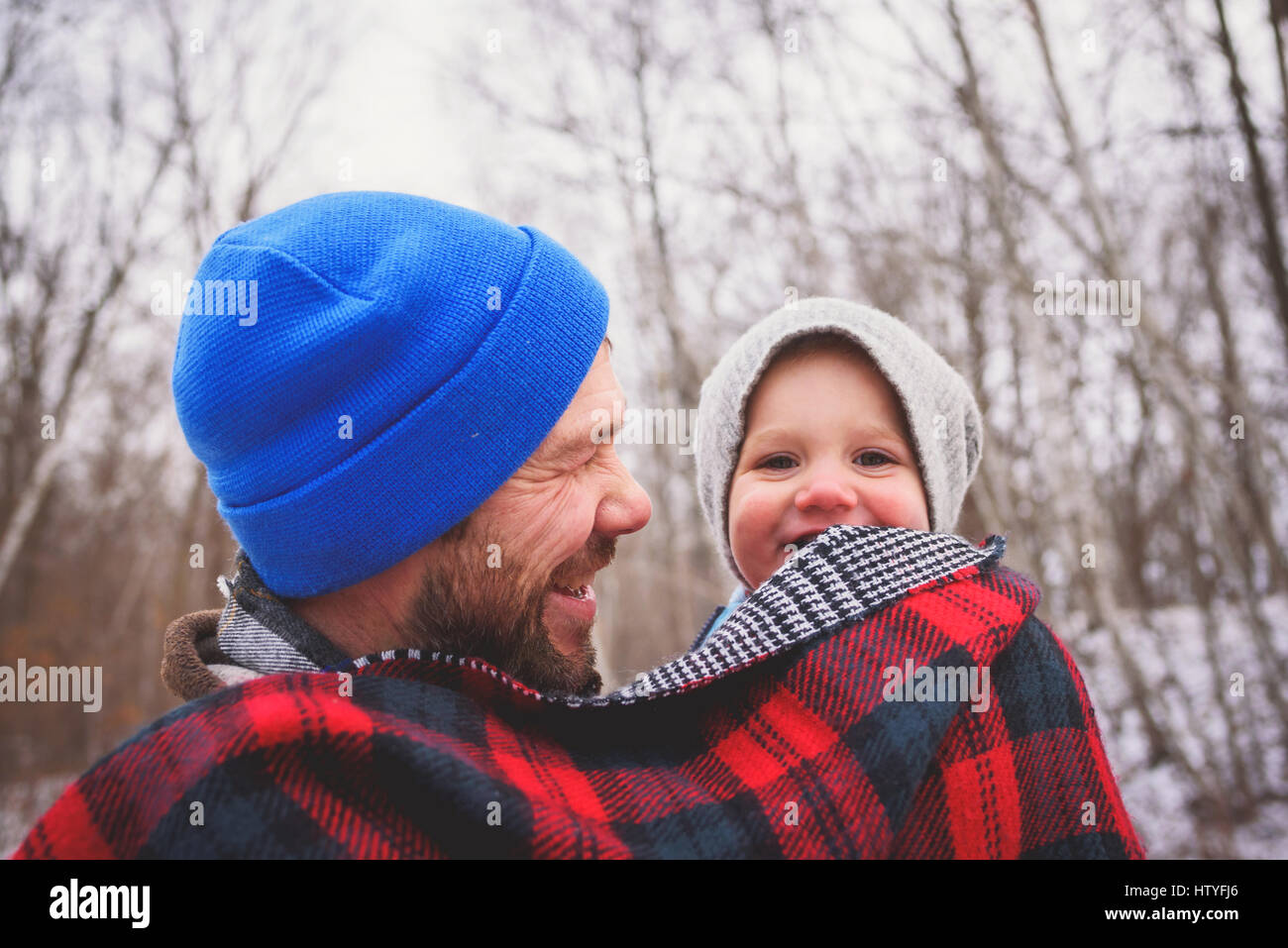 Portrait d'un père portant son bébé fils dans une forêt d'hiver enveloppée dans une couverture Banque D'Images