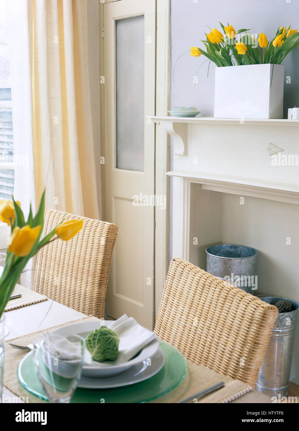 Chaises en osier retour à table avec le blanc et le vert de la vaisselle dans une économie avec salle à manger de style de rideaux à rayures jaune Banque D'Images