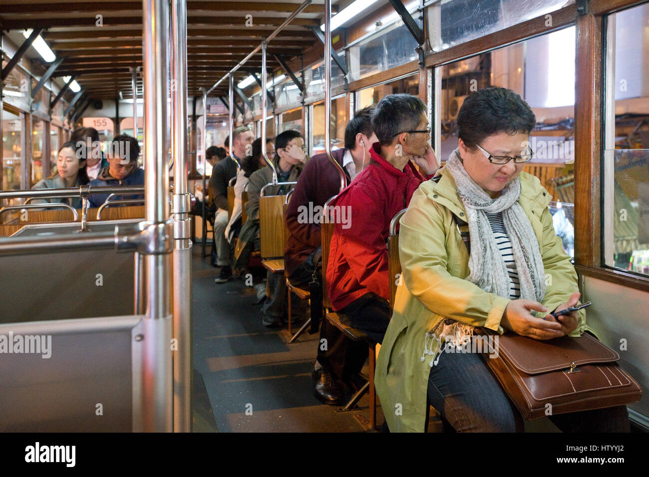 Les passagers assis à l'intérieur d'un tram voyageant le long d'une rue à Causeway Bay avec une femme contrôle de son téléphone mobile. Banque D'Images