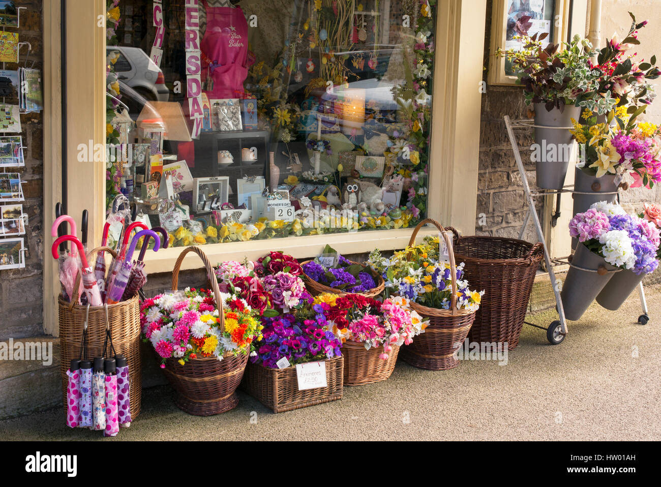 Des paniers en osier coloré de fleurs en plastique à l'extérieur de Country House Boutique cadeaux. Burford, Cotswolds, Oxfordshire, Angleterre Banque D'Images
