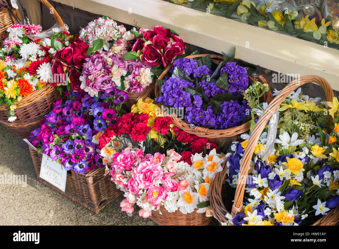 Des paniers en osier coloré de fleurs en plastique à l'extérieur de Country House Boutique cadeaux. Burford, Cotswolds, Oxfordshire, Angleterre Banque D'Images