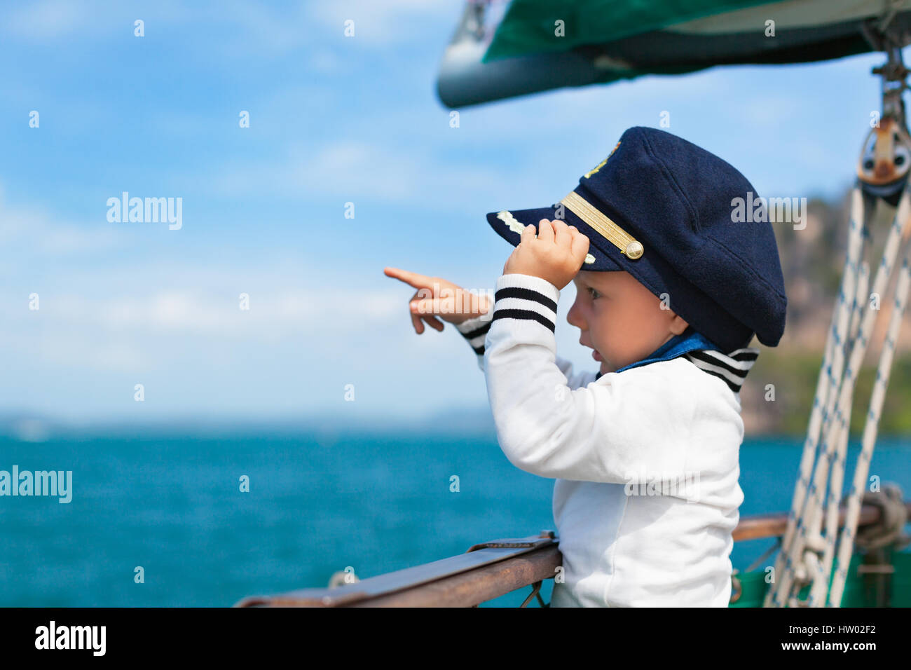 Funny little baby le capitaine à bord du yacht à regarder la mer au large de l'été sur une croisière. Voyage d'aventure, le yachting avec enfant en vacances en famille. Banque D'Images