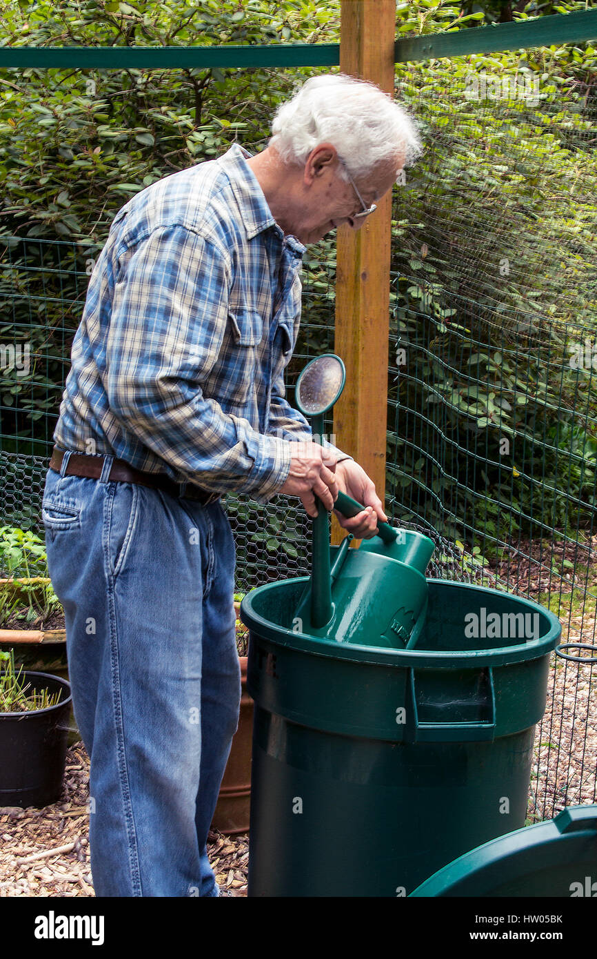 L'homme son arrosoir de remplissage d'une grande poubelle d'eau à côté de  son jardin, à l'ouest de l'État de Washington, USA Photo Stock - Alamy