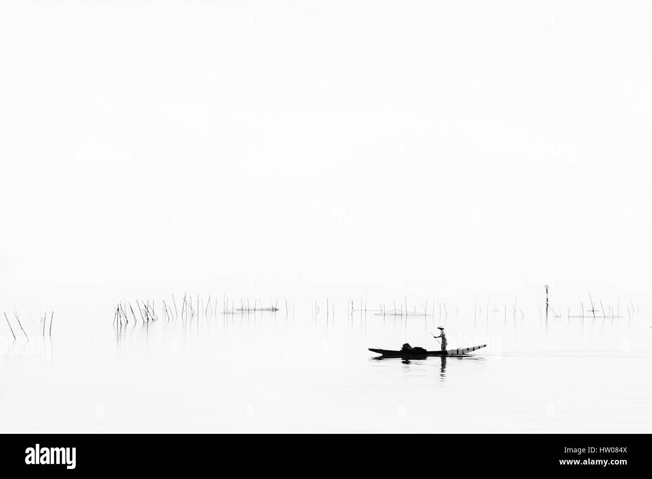 Bateau de pêche traditionnel sur le lac au lever du soleil, le brouillard passant de l'eau - Vietnam Banque D'Images