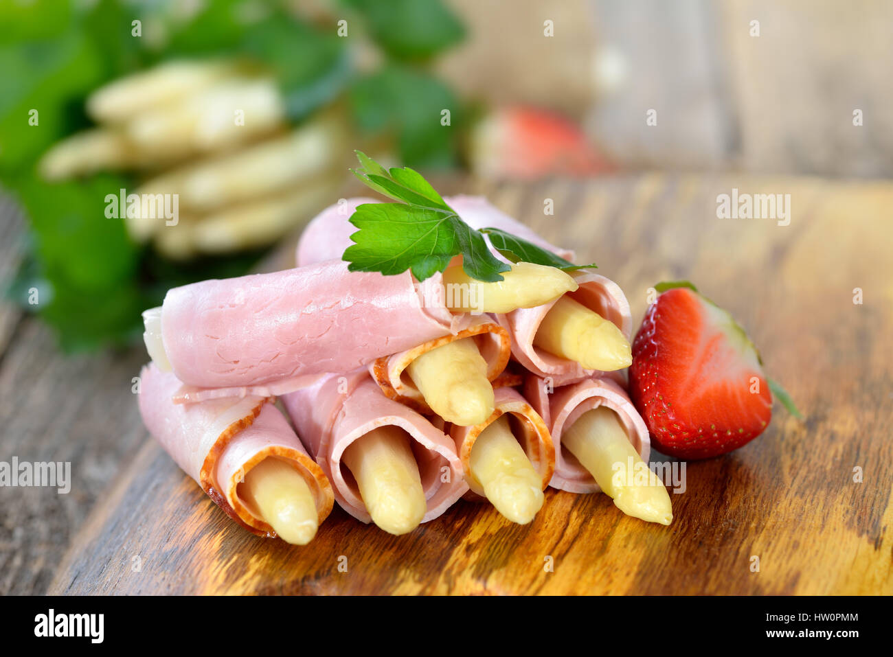 Rouleaux de jambon cuit avec de l'asperge blanche sur une planche en bois avec des fraises Banque D'Images