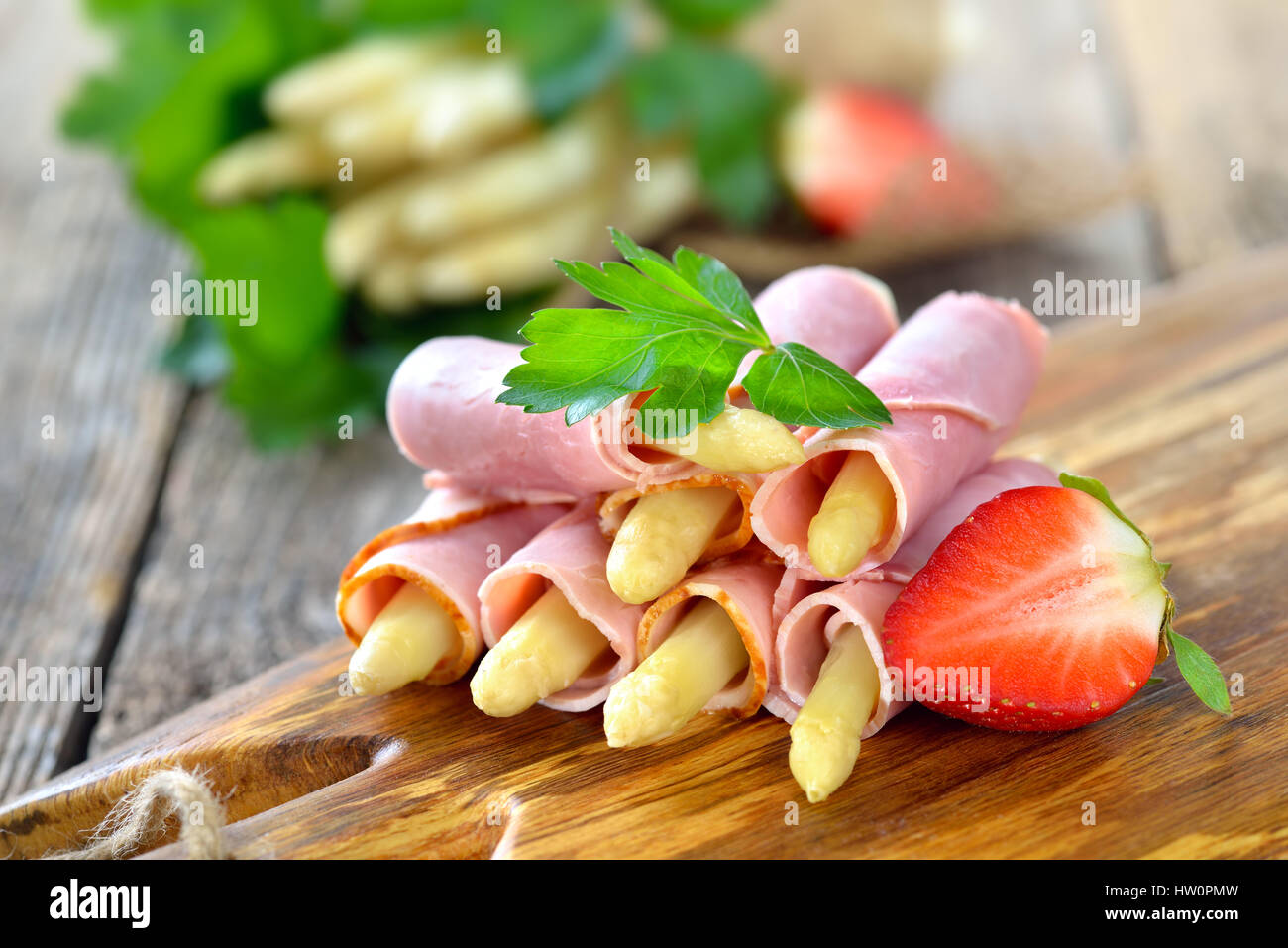 Rouleaux de jambon cuit avec de l'asperge blanche sur une planche en bois avec des fraises Banque D'Images