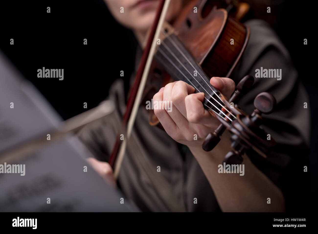 Libre d'une méconnaissable encore de main du joueur tenant un violon tout en jouant. Portrait sur une pièce de musique noire floue score en premier plan Banque D'Images
