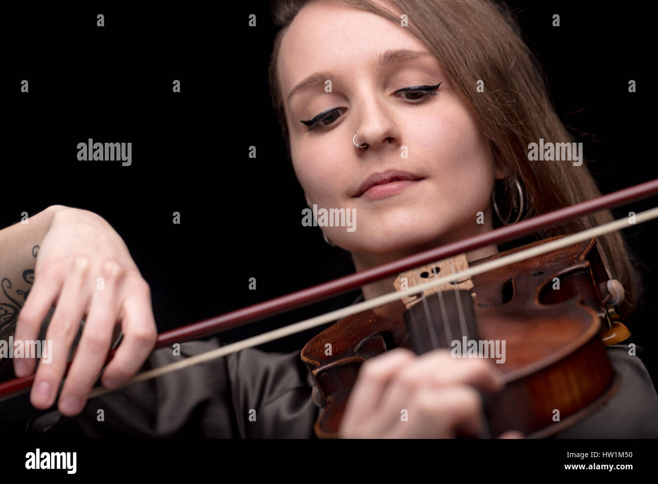 Jeune femme belle violoniste joueur de jouer son instrument sur son épaule holding arc. portrait dans une chambre noire floue en arrière-plan. Concept de c Banque D'Images