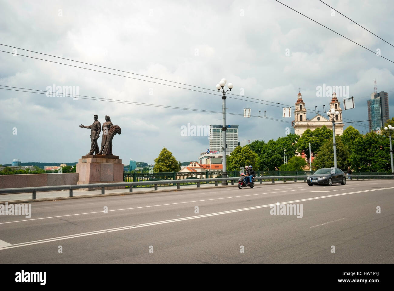 Vue sur pont vert à la circulation et la statue de l'homme et de la femme à l'encontre de ciel nuageux. Banque D'Images