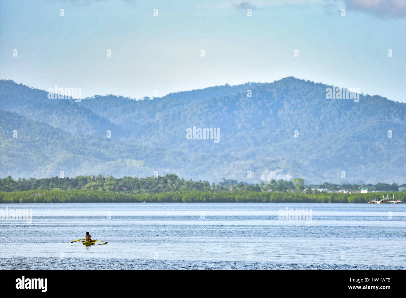 Seul pêcheur philippin dans son bateau de pêche traditionnel sur l'eau avec des collines couvertes d'arbres arrière-plan. Banque D'Images