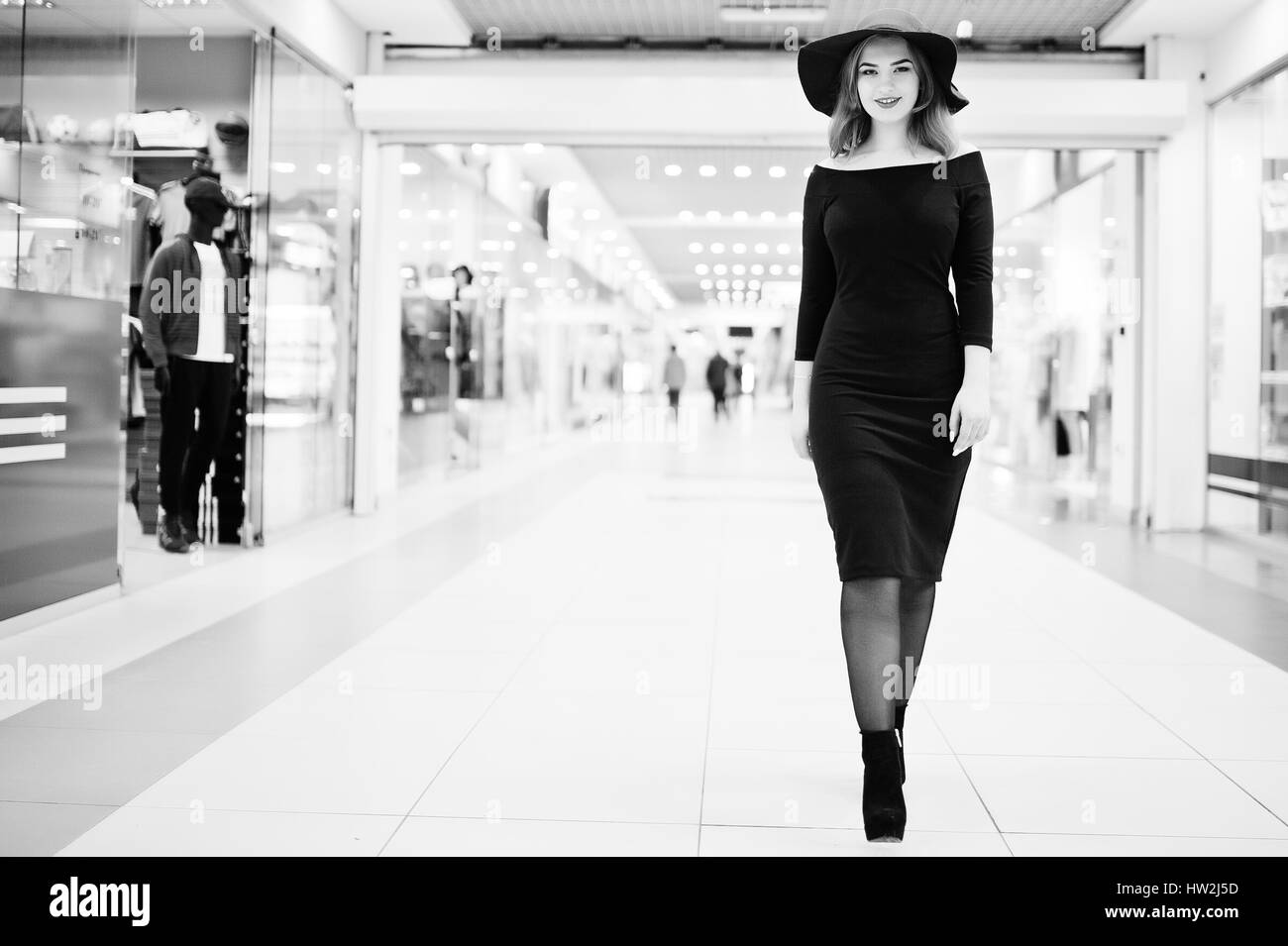 Fille aux cheveux rouges de mode de l'usure sur robe noire et red hat posés au centre commercial du commerce. Photo en noir et blanc. Banque D'Images