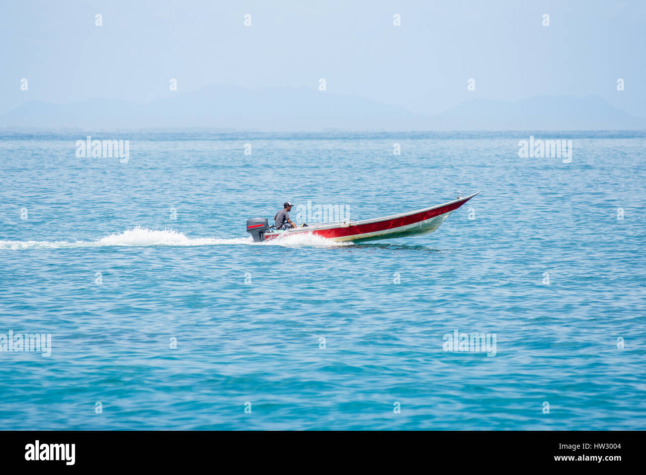 Homme seul dans une embarcation avec moteur hors-bord rapide voyage à travers une mer bleu clair calme. Banque D'Images