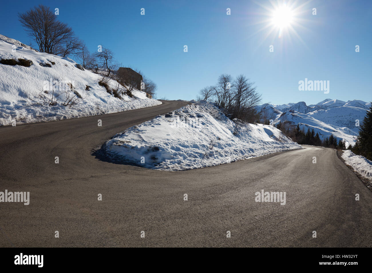 Route de montagne vide courbe avec de la neige sur les côtés, ciel bleu et soleil Banque D'Images