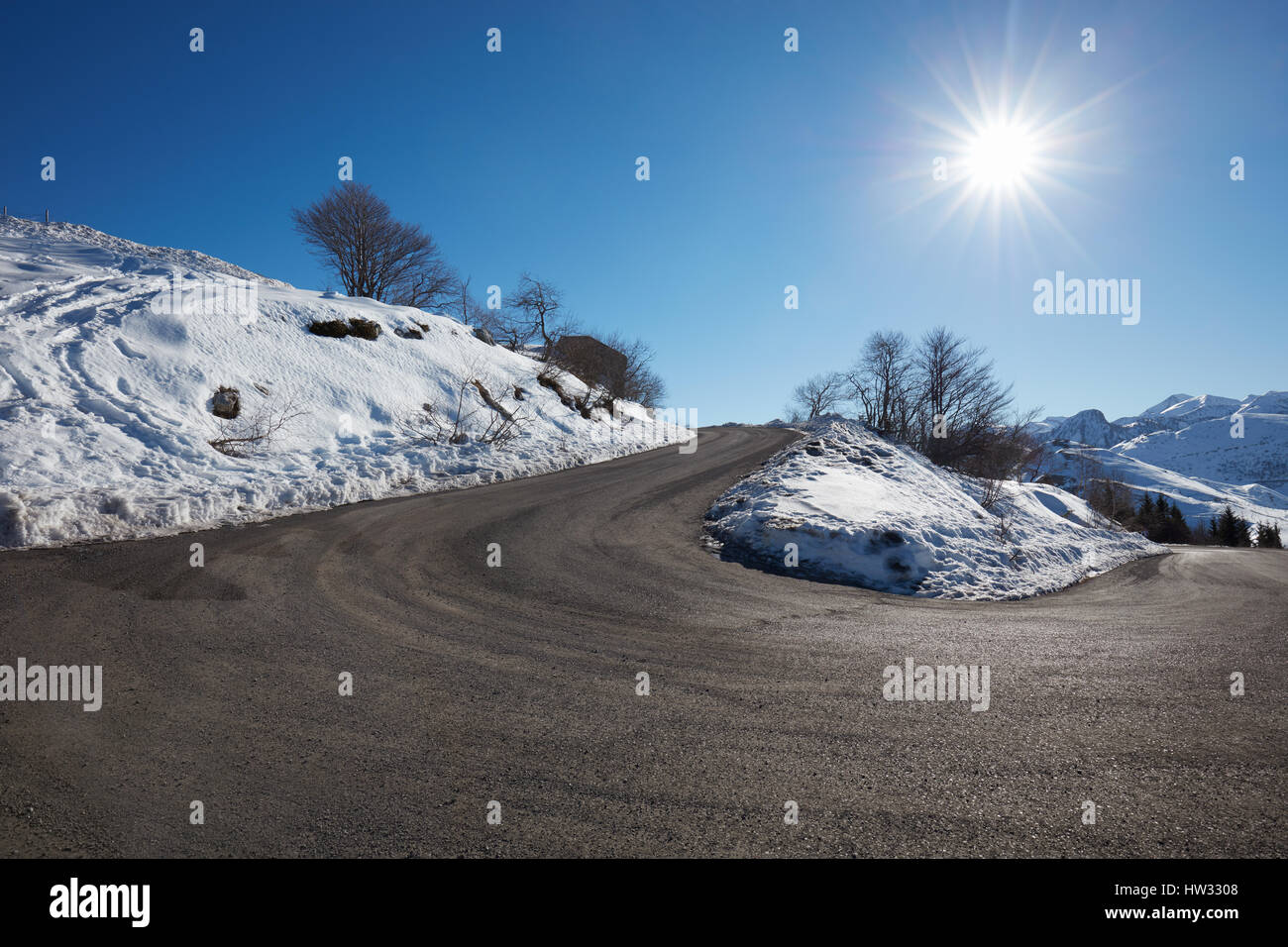 Route de montagne vide courbe sur Alpes avec neige sur côtés, ciel bleu dans une journée ensoleillée Banque D'Images