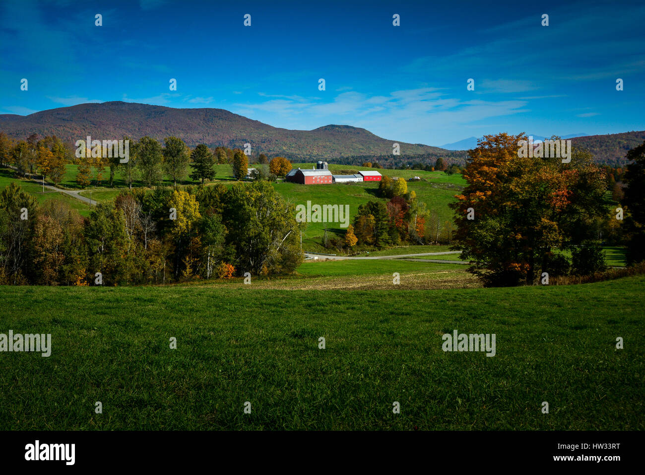 Une ferme pittoresque avec une grange rouge classique nichée parmi les pâturages verts et les montagnes lors d'une journée d'automne ensoleillée dans le nord du Vermont, États-Unis. Banque D'Images