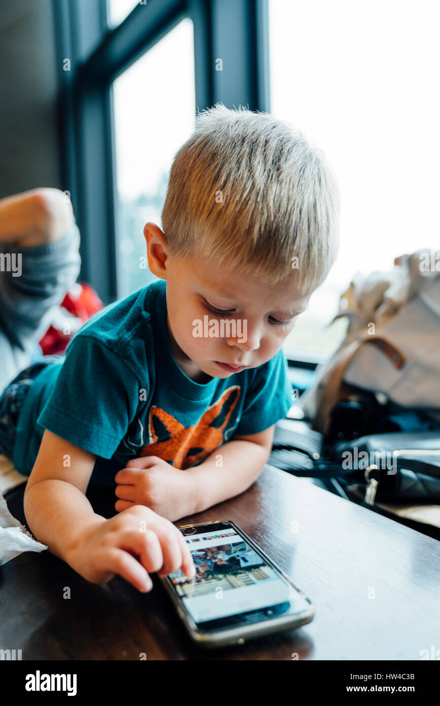 Mixed Race boy laying on table using cell phone Banque D'Images