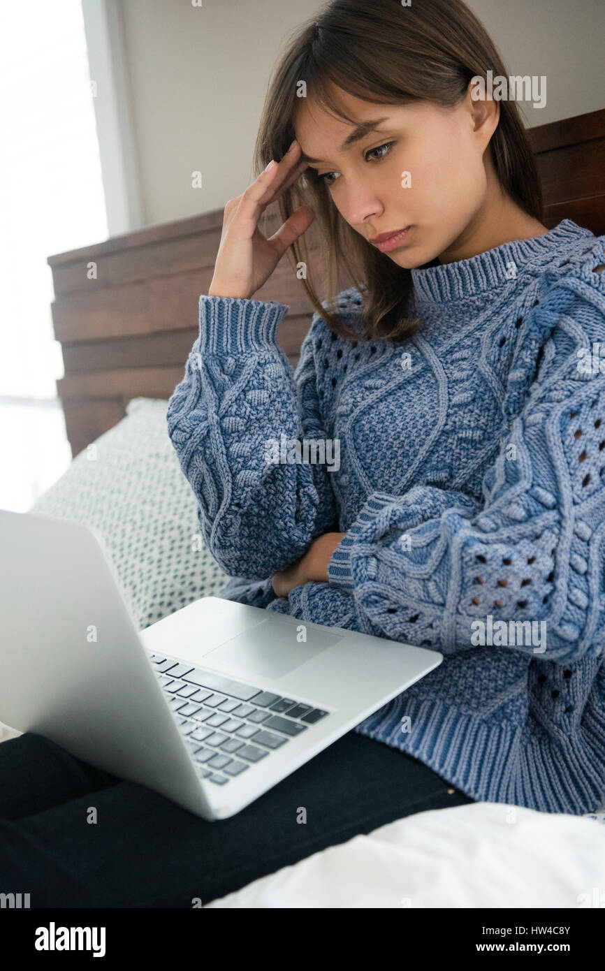 Frustrés Mixed Race woman using laptop in bed Banque D'Images