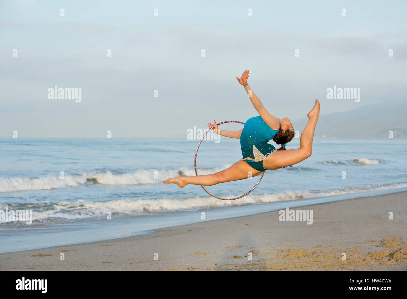 Young gymnast jumping with hoop on beach Banque D'Images