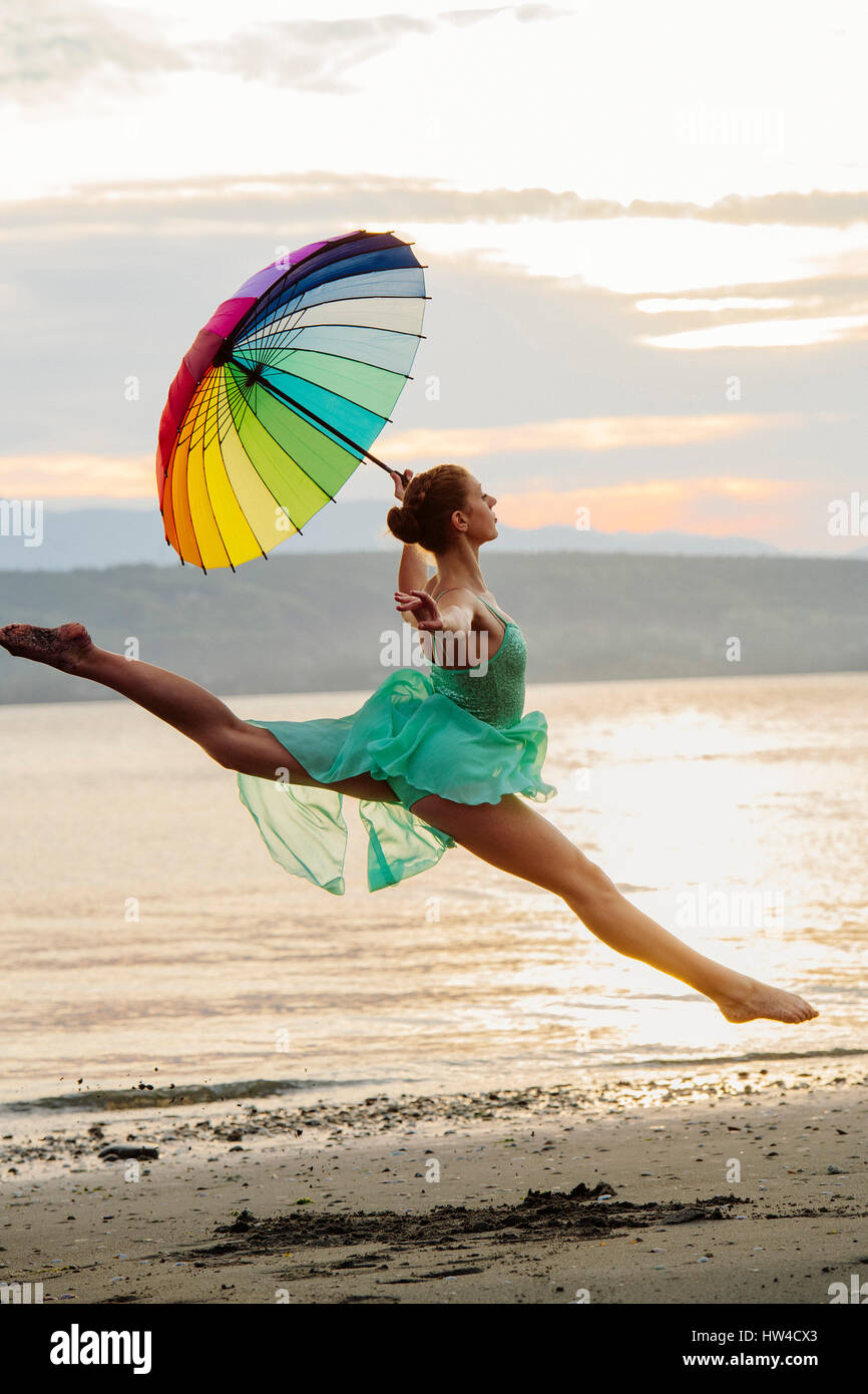 Caucasian ballerina sautant avec parapluie multicolore on beach Banque D'Images