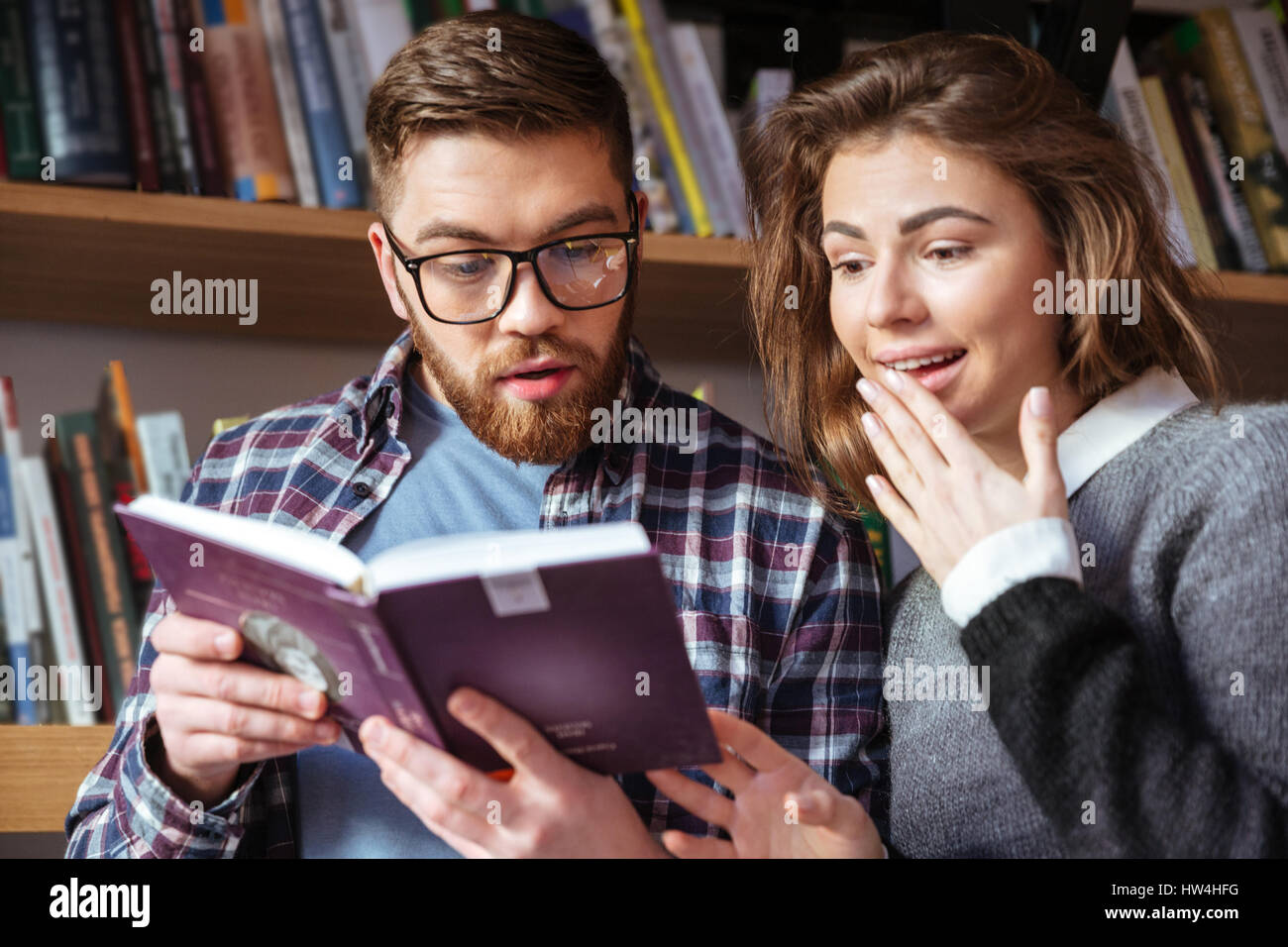 Deux étudiants intelligents la lecture et l'étude lors de la recherche de la bibliothèque par des livres sur les étagères Banque D'Images