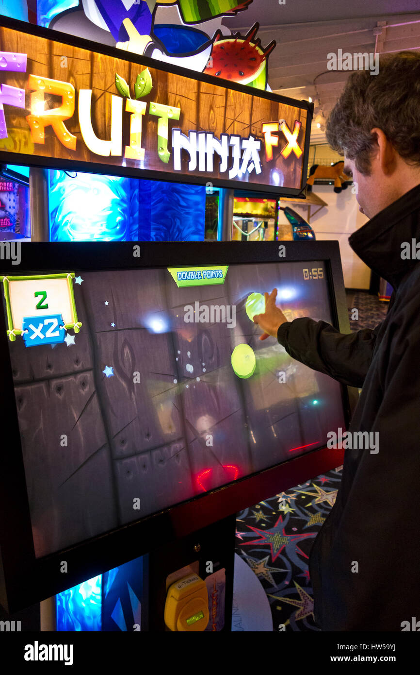 L'homme en balayant l'écran pendant la lecture Fruit Ninja FX jeu dans une salle de jeux vidéo à Long Beach, Washington. Banque D'Images