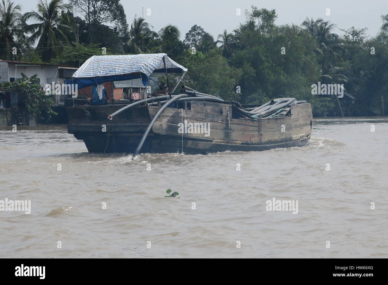 Mékong en Indochine, il vous suffit de bateau en bois sur la rivière sale avec des maisons sur des piliers colorés voile unique. Banque D'Images