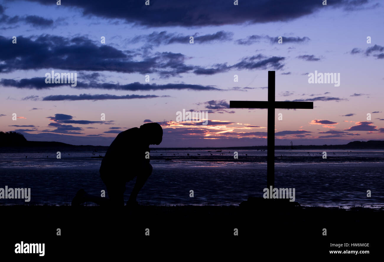 La journée se termine comme un homme à genoux prier devant une croix. Banque D'Images