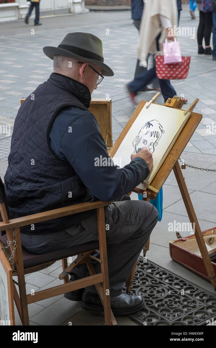 Vue sur l'épaule d'un homme artiste de rue, la création d'une caricature dessin (dessin animé) d'un jeune garçon - King's Square, York, North Yorkshire, Angleterre. Banque D'Images