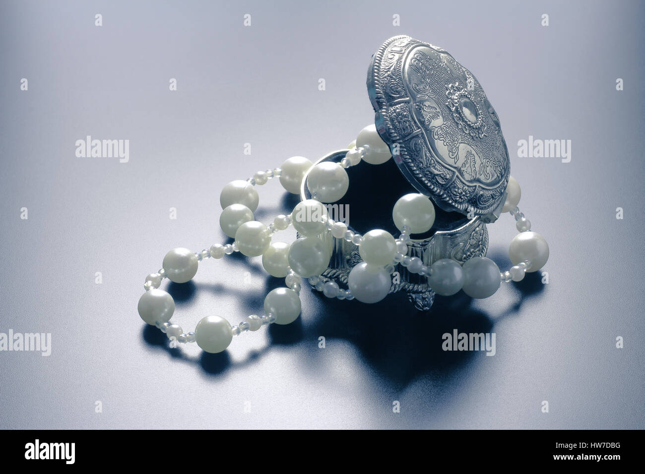 Photo d'une boîte de bijoux en argent avec perles blanches tourné avec projecteurs et fond noir Banque D'Images