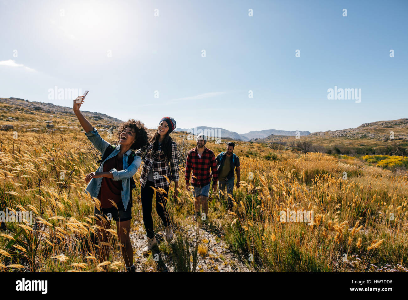 Groupe d'amis prendre photo sur pied. Les jeunes, hommes et femmes, randonnées en campagne et en tenant avec selfies téléphone intelligent. Banque D'Images