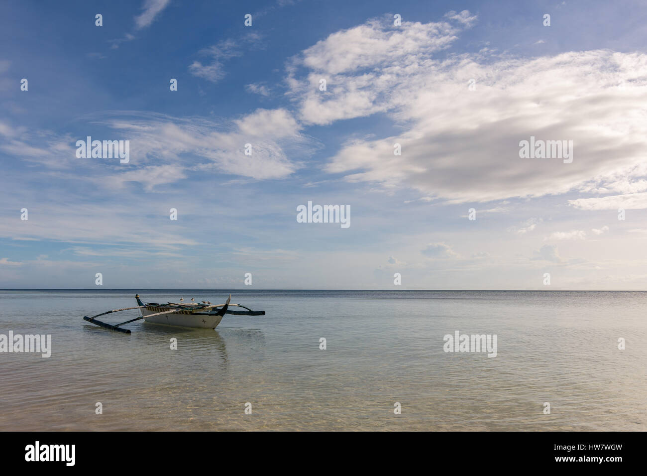 Un pêcheur philippin de la pompe de base du bateau flottant sur un vide toujours calme mer tropicale avec les mouettes en appui sur ses stabilisateurs. Banque D'Images